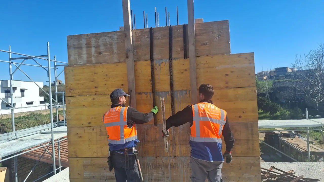 Due persone con gilet arancione davanti a casseri in legno.